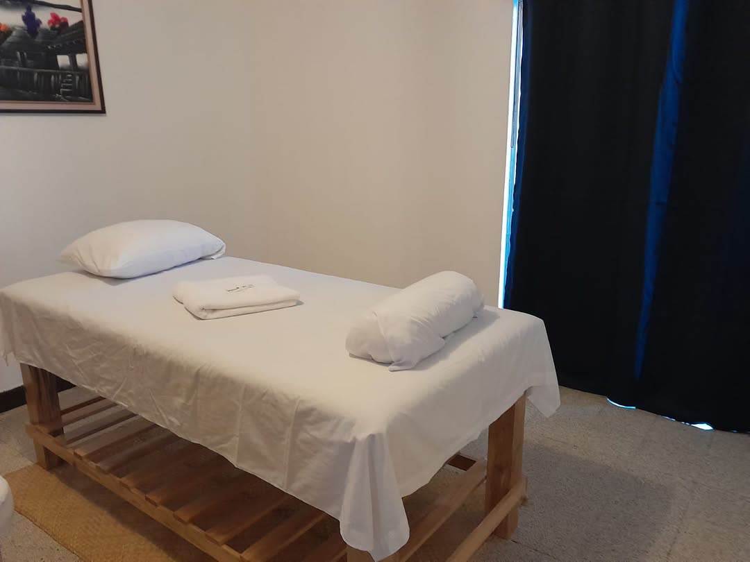 Cabina de masaje de Heavenly Massage: camilla de madera con sábanas blancas, almohada, toalla y cojín